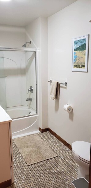 A bathroom with a glass-enclosed shower, a toilet, a roll of toilet paper, and a poster on the wall. - Waterfront, Panoramic Views! White Star Point (Brussels)