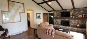 A living room with a stone fireplace, a sofa, a map on the wall, and a television. - Waterfront, Panoramic Views! White Star Point (Brussels)