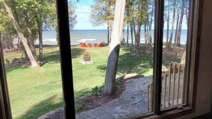 Vista a través de una ventana que muestra un césped, árboles y una terraza de madera.