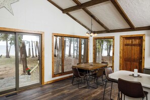 A room with a wooden table and chairs, large windows with a view of trees, and a wooden door. - Waterfront, Panoramic Views! White Star Point (Brussels)