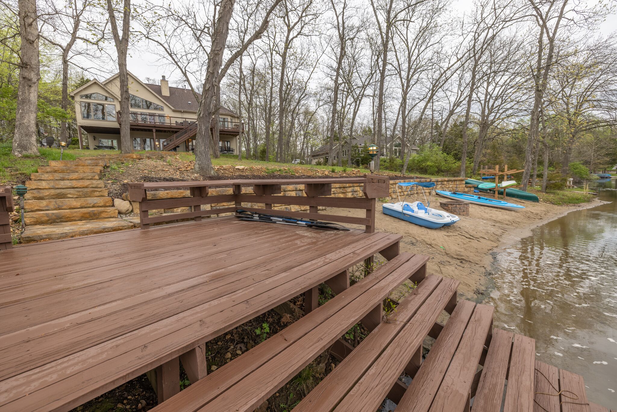 Eine Holzterrasse mit Bänken, die auf einen Fluss mit Bäumen und einem Haus im Hintergrund blickt.