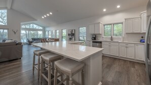 Een ruime keuken met een groot eiland, witte kasten en een zithoek met een bank en stoelen.