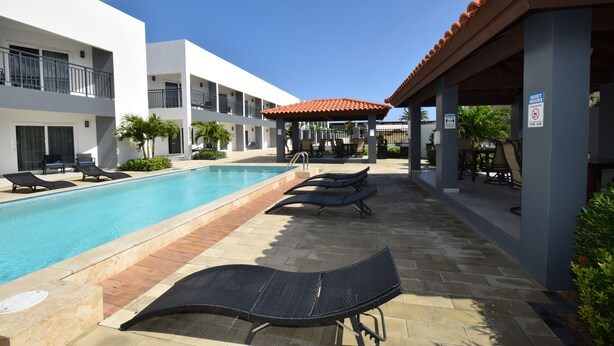 A pool area with lounge chairs, a covered seating area, and a sign indicating quiet hours. - Arena Condos Aruba 250 m to Eagle beach Aruba (Noord)