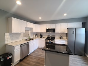 A modern kitchen with white cabinetry, a stainless steel refrigerator, and a black countertop island.