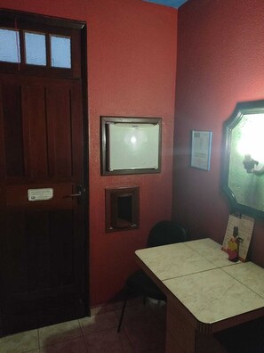 A room with a wooden door, a small table, and a mirror on the wall.