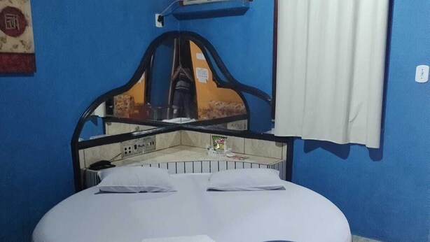 A circular bed with a headboard, a white curtain, and a small air conditioning unit on the wall. - Pousada Devaneios (Ananindeua)