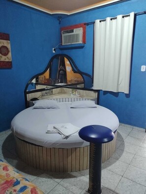 A circular bed with a headboard, a white curtain, and a small air conditioning unit on the wall.