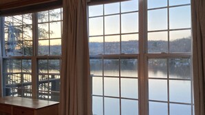 A room with a bed, a desk, and a large window overlooking a lake. - Cozy Lakefront Bungalow w firepit/dock/kayaks (Plymouth)