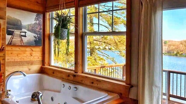 A wooden cabin with a large window, a wooden deck, and a bathtub. - Cozy Lakefront Bungalow w firepit/dock/kayaks (Plymouth)