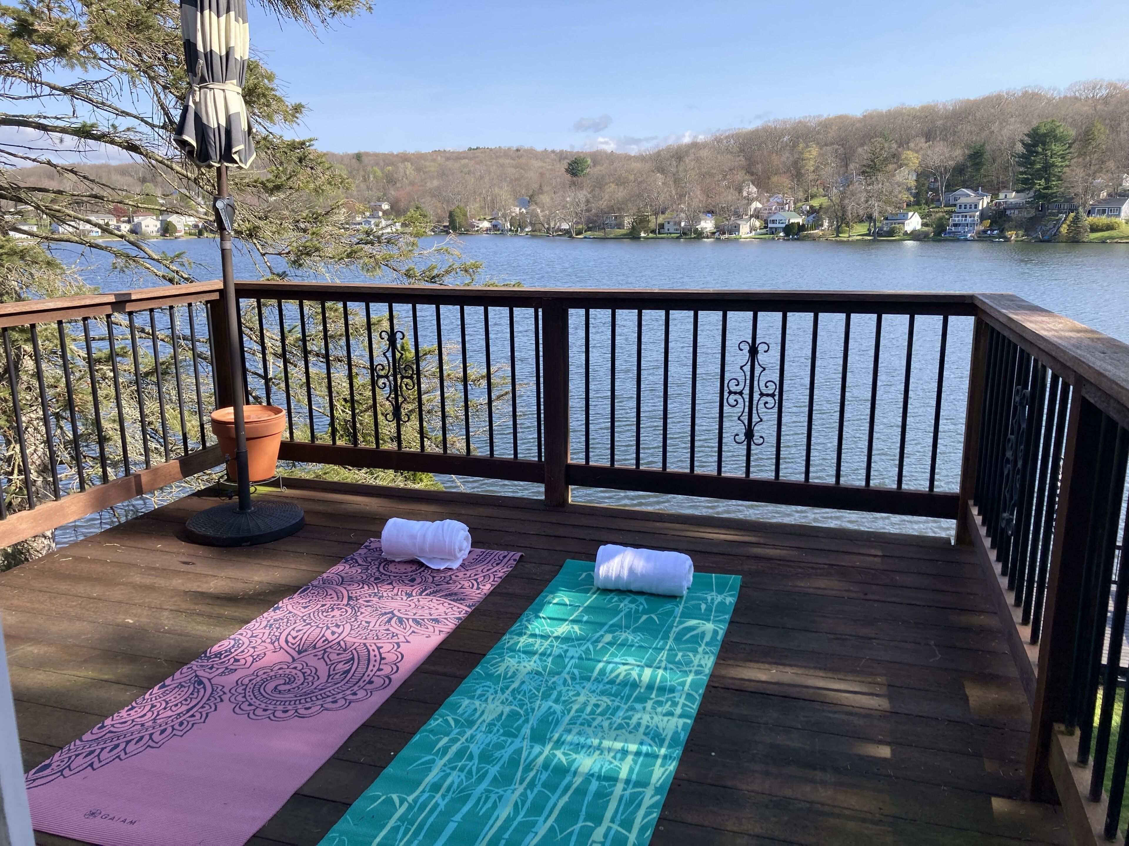Une terrasse en bois avec deux tapis de yoga, une plante en pot et un parasol décoratif.