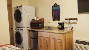 Una cocina compacta con lavadora, microondas, cafetera y un lavamanos pequeño.