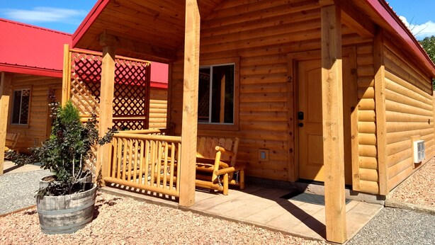 Una cabaña de madera con techo rojo, un porche con celosía y un pequeño jardín.