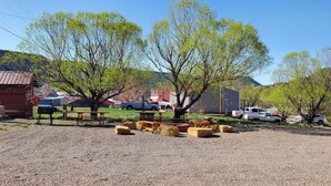Entorno rural con zona de estacionamiento de grava, mesas de picnic y un edificio rojo.