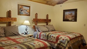 Una habitación con dos camas, cabeceros de madera, una mesita de noche con lámpara y dos cuadros enmarcados en las paredes.