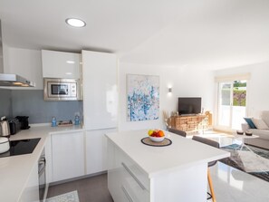A modern kitchen with white cabinetry, a built-in microwave, and a fruit bowl on the island.