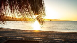 Una spiaggia al tramonto con una sedia a sdraio in vimini rivolta verso l'oceano.