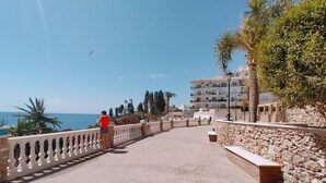 A paved walkway with a white balustrade, leading to a view of the sea and a building with multiple balconies. - Nerja Sun Apartment Bahía 17 (Nerja)