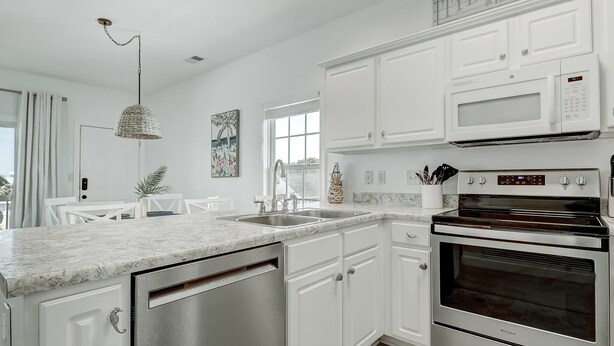 A modern kitchen with white cabinetry, a built-in microwave, and a stainless steel dishwasher. - South Beach Condo, Porch Swing with Ocean View (Tybee Island)