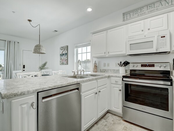 A modern kitchen with white cabinetry, a built-in microwave, and a stainless steel dishwasher. - South Beach Condo, Porch Swing with Ocean View (Tybee Island)