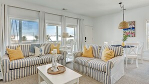 A spacious living room with striped sofas, a white coffee table, and a ceiling fan. - South Beach Condo, Porch Swing with Ocean View (Tybee Island)
