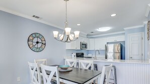 A modern kitchen with white cabinetry, a central island, and a dining area with white chairs. - South End Tybee Getaway, Short Walk to Beach (Tybee Island)