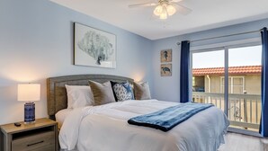 A bedroom with a bed, a nightstand, a lamp, a ceiling fan, and artwork on the walls. - South End Tybee Getaway, Short Walk to Beach (Tybee Island)