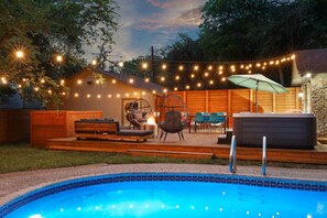 Ein Garten mit Schwimmbecken, Holzterrasse, Gartenmöbeln und Lichterketten.