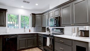 A modern kitchen with dark cabinets, stainless steel appliances, and a dishwasher. - Pool~Hottub~Yoga Gym~Game Room~Fire Pit (Austin)