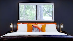 A bedroom with a large bed, two bedside lamps, a window with a view of trees, and a dark wall. - Pool~Hottub~Yoga Gym~Game Room~Fire Pit (Austin)