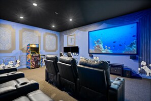 Un cine en casa con una pantalla grande, asientos cómodos y un mural en la pared.