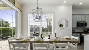 Comedor con una gran mesa dispuesta para seis comensales, sillas blancas, lámpara colgante y vistas amplias a través de grandes ventanales.