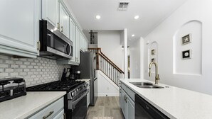 Una cocina con armarios blancos, estufa de acero inoxidable, microondas y un lavamanos.