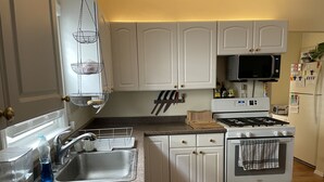 Una cuina amb armaris blancs, un rentaplat de metall inoxidable, un microones, una placa de cocció i un frigorífic.