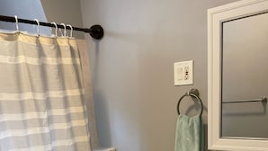 Un bany amb cortina de dutxa estriada, un vàter, un lavabo amb dispensador de sabó i un mirall amb una tovallola penjada a la paret.