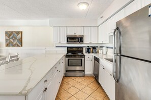 Enjoy cooking in this well-equipped kitchen with a gas stove, microwave, and refrigerator, complemented by a large island and white cabinetry.