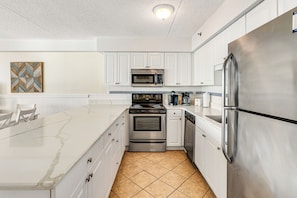 Enjoy cooking in this well-equipped kitchen with a gas stove, microwave, and refrigerator, complemented by a large island and white cabinetry.