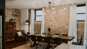 Ein Essbereich mit Backsteinwand, einem Holztisch, schwarzen Stühlen und einem Kronleuchter.