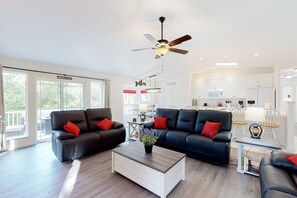 A modern living room with two black leather sofas, a white coffee table, and a ceiling fan.