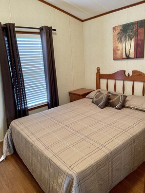 A bedroom with a bed, a nightstand, a window with curtains, and a painting on the wall. - Delightful 3 bedroom cottage in Sherkson Shores beach Retreat! (Port Colborne)