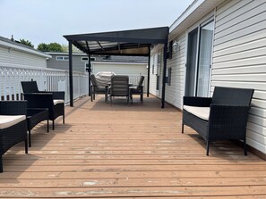 A covered outdoor deck with wicker furniture and a table, adjacent to a building with white siding. - Delightful 3 bedroom cottage in Sherkson Shores beach Retreat! (Port Colborne)