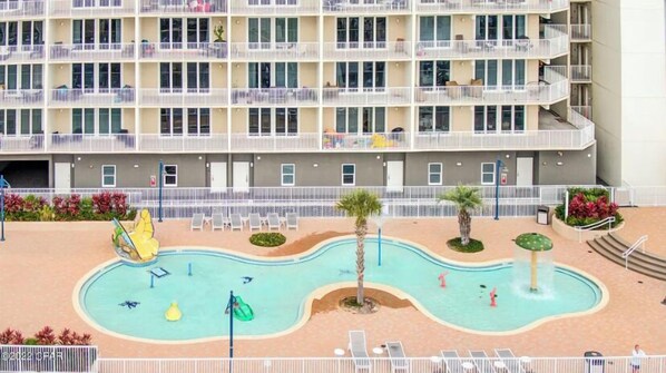 Un hotel de varios pisos con una zona de piscina que incluye un tobogán, palmeras y tumbonas.