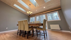 Een eethoek met een houten plafond, dakramen, een kroonluchter en een tafel met stoelen.