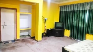 A room with yellow walls, a bed, a television on a cabinet, and a door. - Organic Farm with kitchen, AC rooms, Pet-friendly 7 Kms from the city (Jhansi)