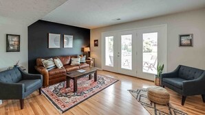 Un salon avec un mur d’accent de couleur sombre, un canapé en cuir, deux fauteuils, une table basse et une grande fenêtre donnant sur l’extérieur.