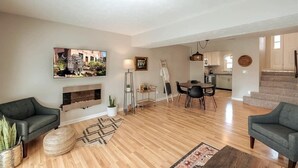 Un salon moderne avec une cheminée, un coin repas et une cuisine en arrière-plan.