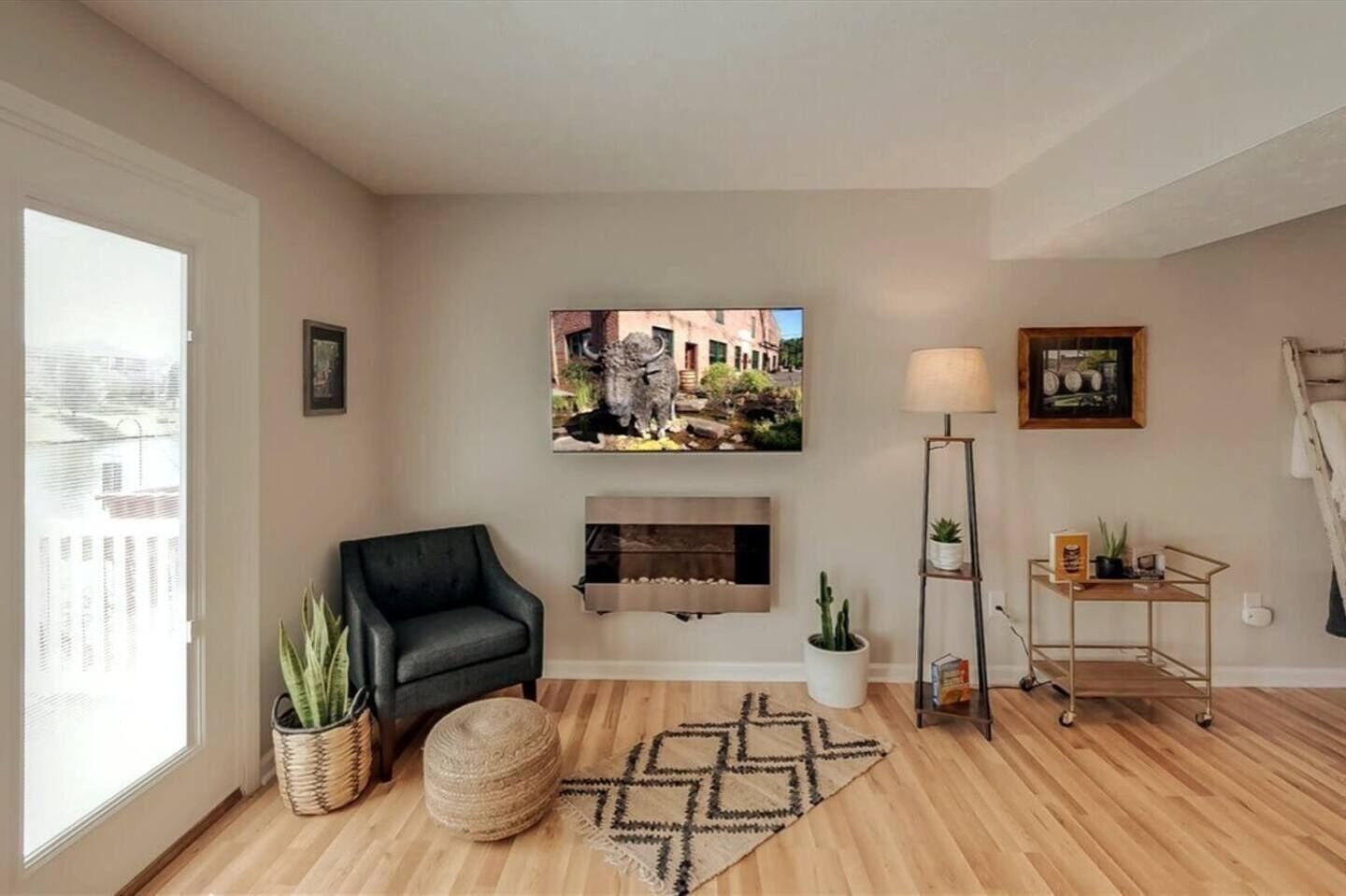 Un salón con chimenea, un sofá de cuero negro, una alfombra, una lámpara de pie y un televisor montado en la pared.