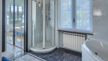 A modern bathroom with a glass shower enclosure, a bathtub, and a window providing natural light.