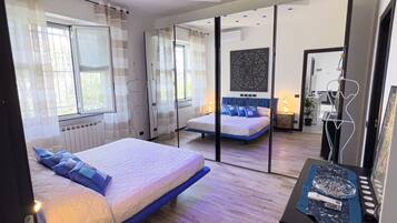 A modern bedroom with a large bed, a second smaller bed, a mirror, and a bedside table with a decorative item.