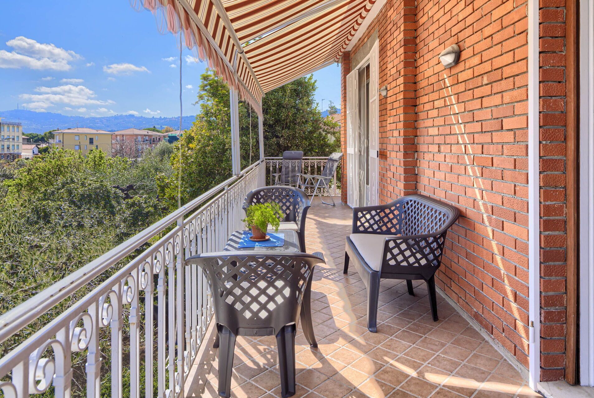 A balcony with two chairs and a table, a potted plant, and a view of a cityscape and mountains.