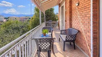 A balcony with two chairs and a table, a potted plant, and a view of a cityscape and mountains.